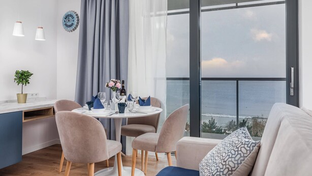 A modern dining area with a round table set for four, a view of the ocean, and a balcony with a view of the sea.