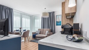 A modern living room with a large window, a sofa, a coffee machine, and a dining area.