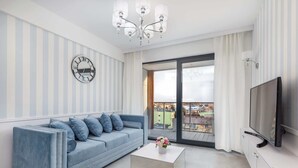 A modern living room with a sofa, a coffee table, a TV, a chandelier, and a large window with a view.