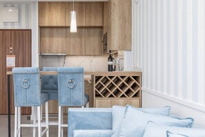 Une cuisine moderne avec des meubles en bois, un meuble à bouteilles et un coin bar agrémenté de deux chaises bleues.