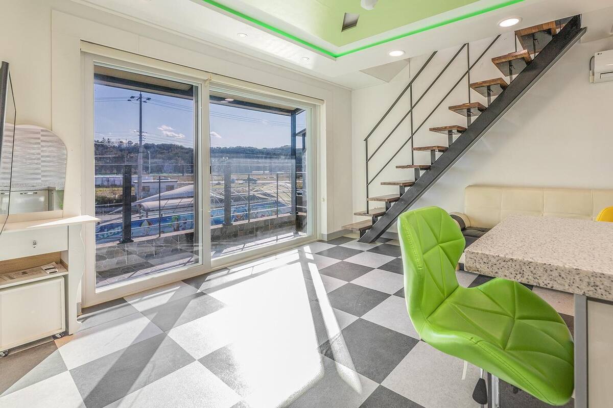 Una cocina moderna con piso a cuadros, una silla verde brillante y una escalera que sube a un nivel superior.