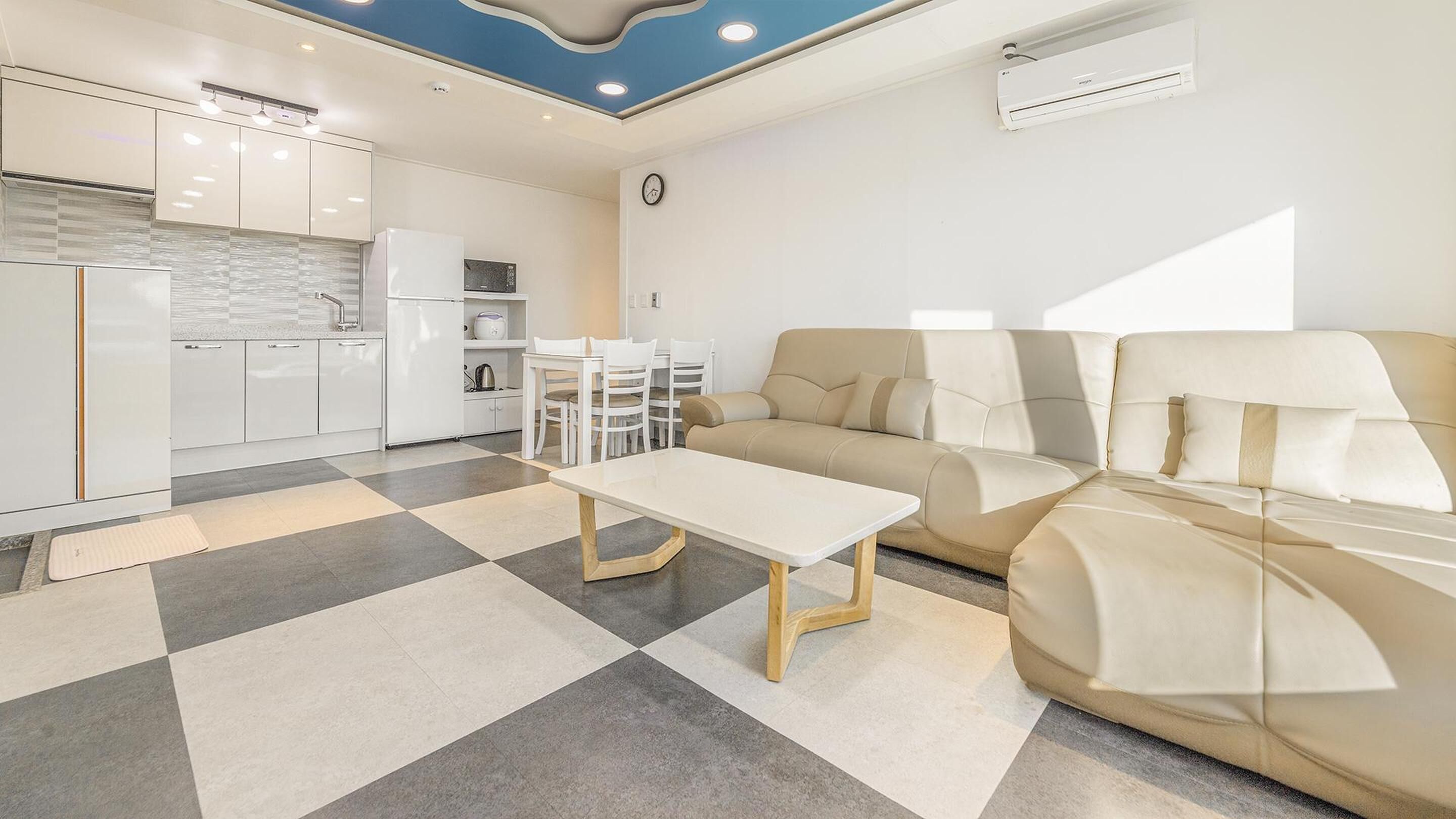 A modern living room with a sofa, a dining table, and a kitchen area with white cabinets and appliances.