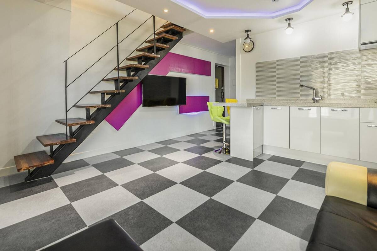 Una cocina moderna con suelo a cuadros, una escalera de madera y una zona de bar con una silla de neón.