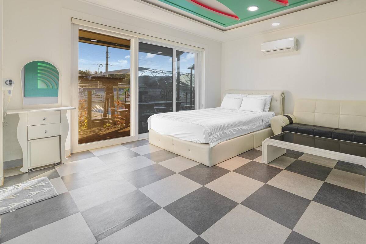 Un dormitorio con cama, sofá, escritorio y un amplio ventanal.