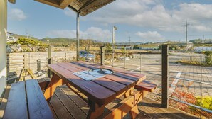 Una mesa de picnic de madera con una placa metálica, ubicada sobre una terraza de madera con barandilla de metal.