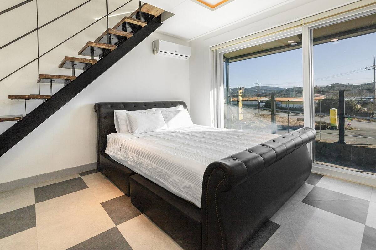 Un dormitorio con una cama, una escalera y un ventanal con vistas al exterior.