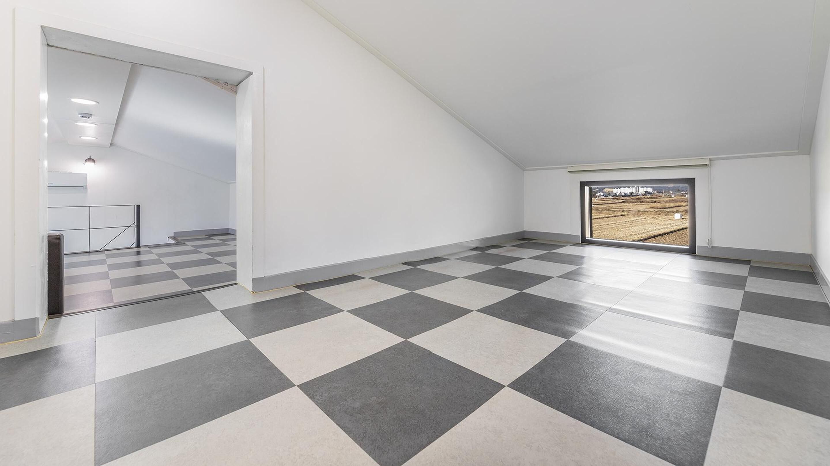 A spacious room with a checkered floor, a large window with a view of a field, and a staircase leading to another level.