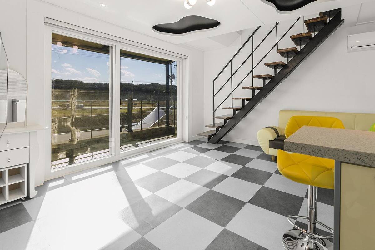 Una cocina moderna con piso a cuadros, un sofá amarillo y una escalera que conduce a un balcón.