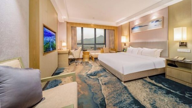 A hotel room with a large bed, a desk, a chair, and a view of the mountains through the window. - Ruijiang International Hotel (Sandu)
