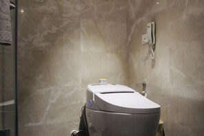 Un baño moderno con pared de mármol, inodoro y secamanos adherido a la pared.