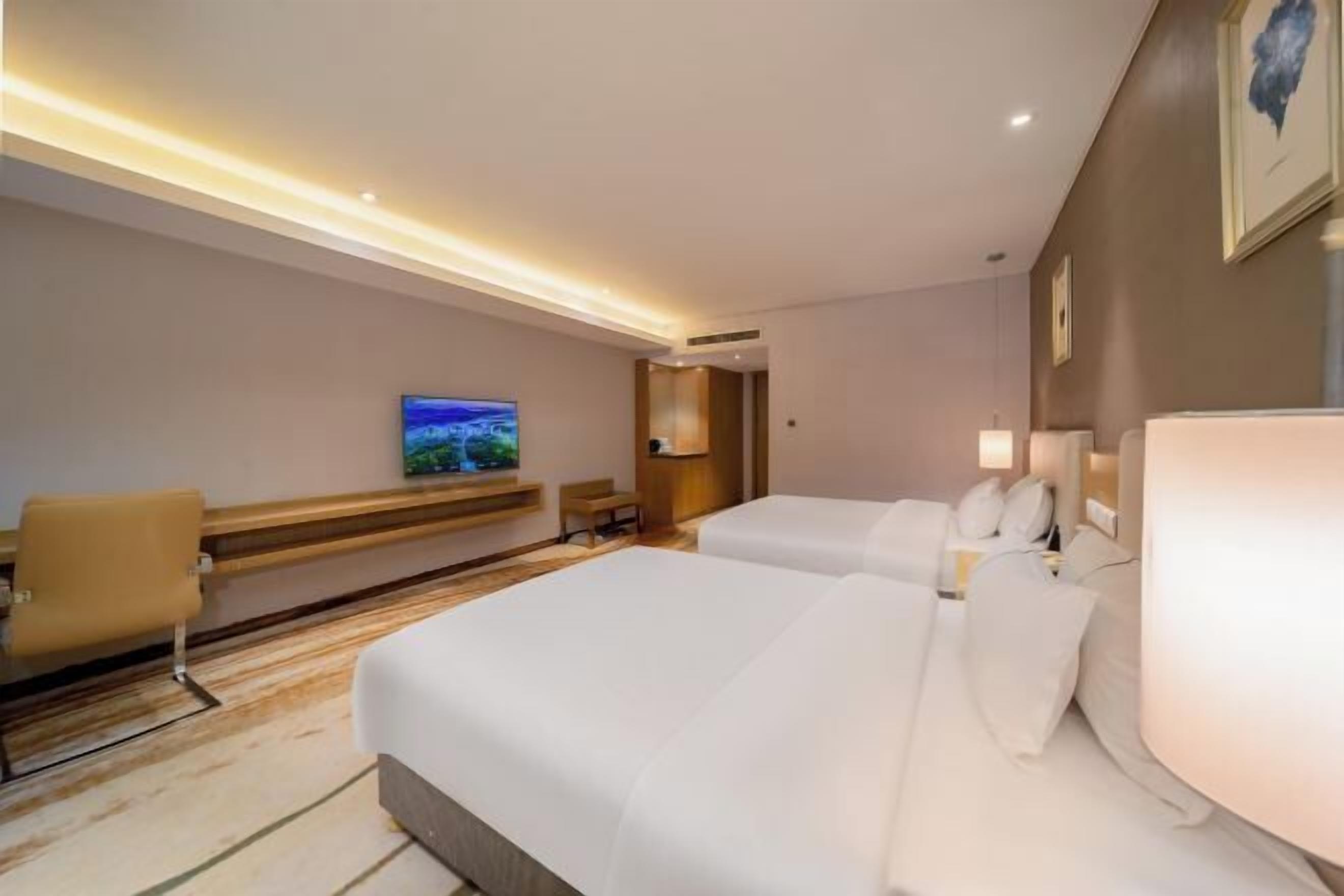 Habitación de hotel con dos camas, televisor, escritorio y una silla.