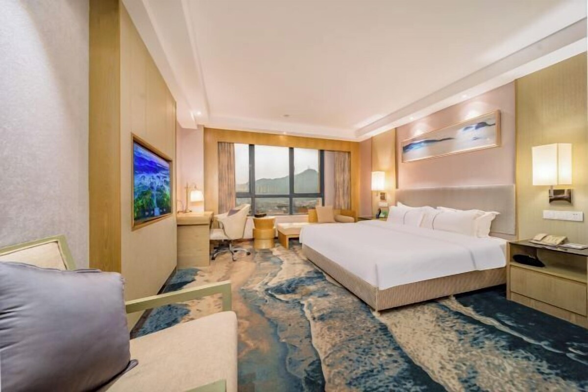 A hotel room with a large bed, a desk, a chair, a sofa, and a view of the mountains through the window.