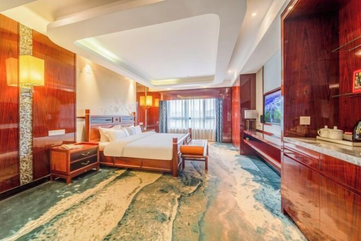 A hotel room with a bed, bedside table, lamp, and a large window.