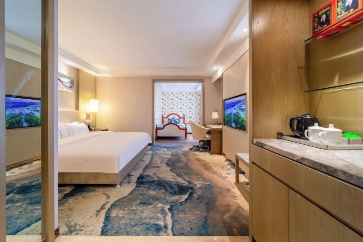A hotel room with a bed, a desk, a chair, a television, a coffee maker, and a bathroom with a shower curtain.