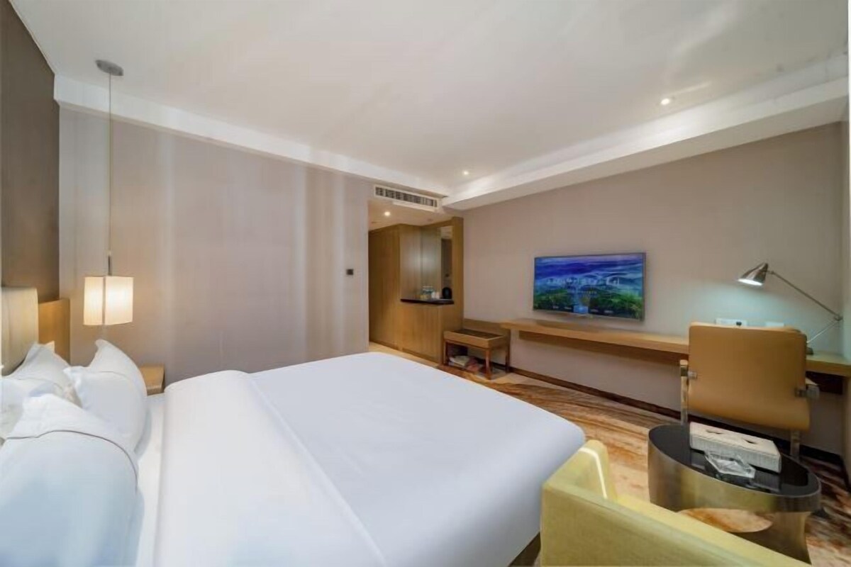 A hotel room with a large bed, a desk, a chair, a TV, and a painting on the wall.