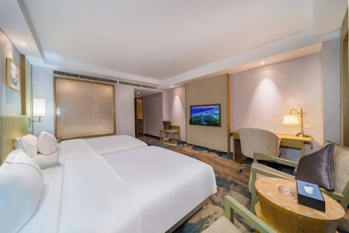 A hotel room with a large bed, a television, a desk with a lamp, and a chair.