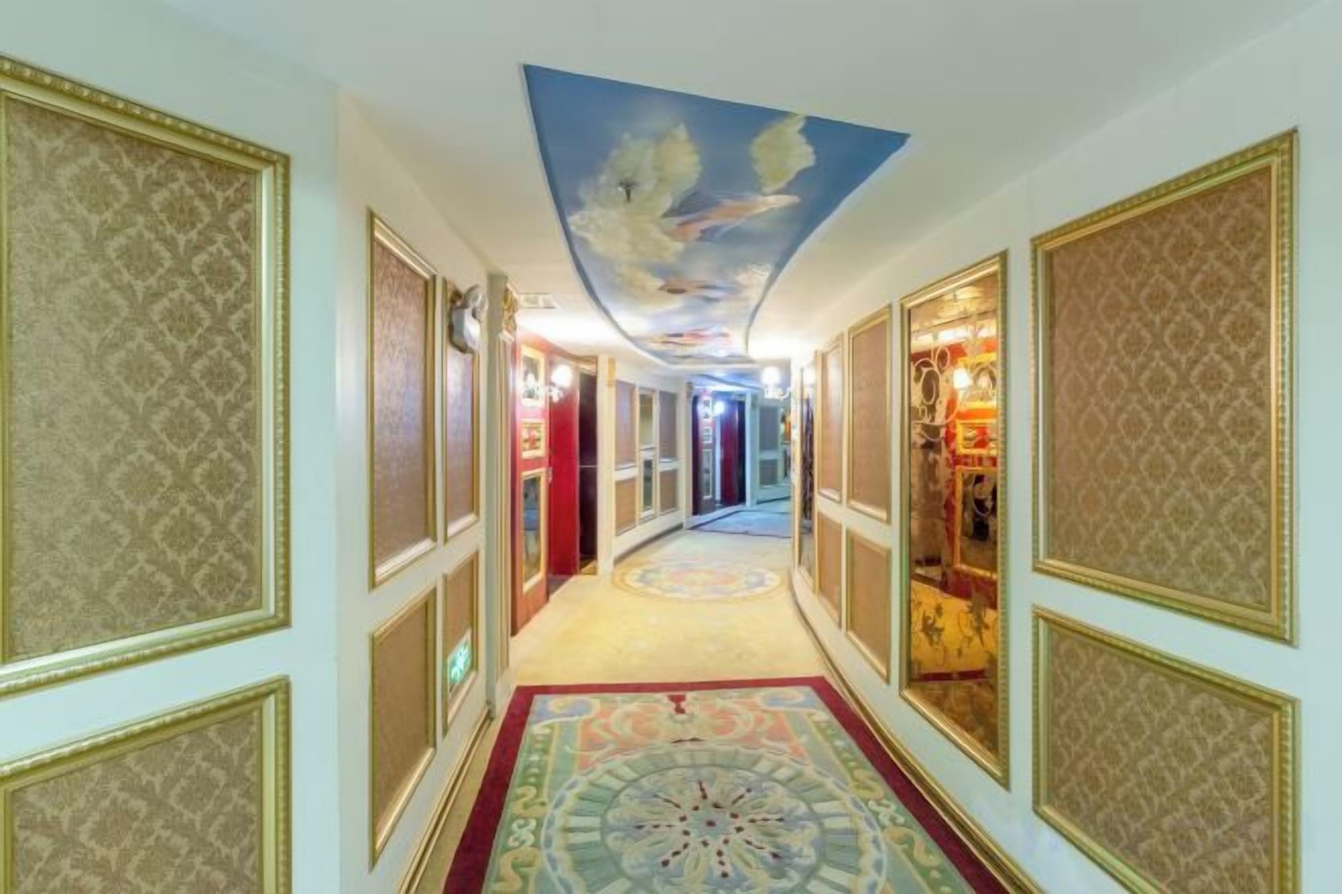Un corridoio con pareti decorate da motivi, un soffitto ornato e un pavimento rivestito di moquette.