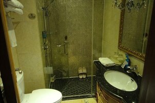 Un baño con ducha compartimentada por vidrio, inodoro blanco y lavamanos negro con espejo superior.