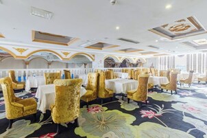 A hotel dining area with tables and chairs, a floral carpet, and a ceiling with decorative elements.