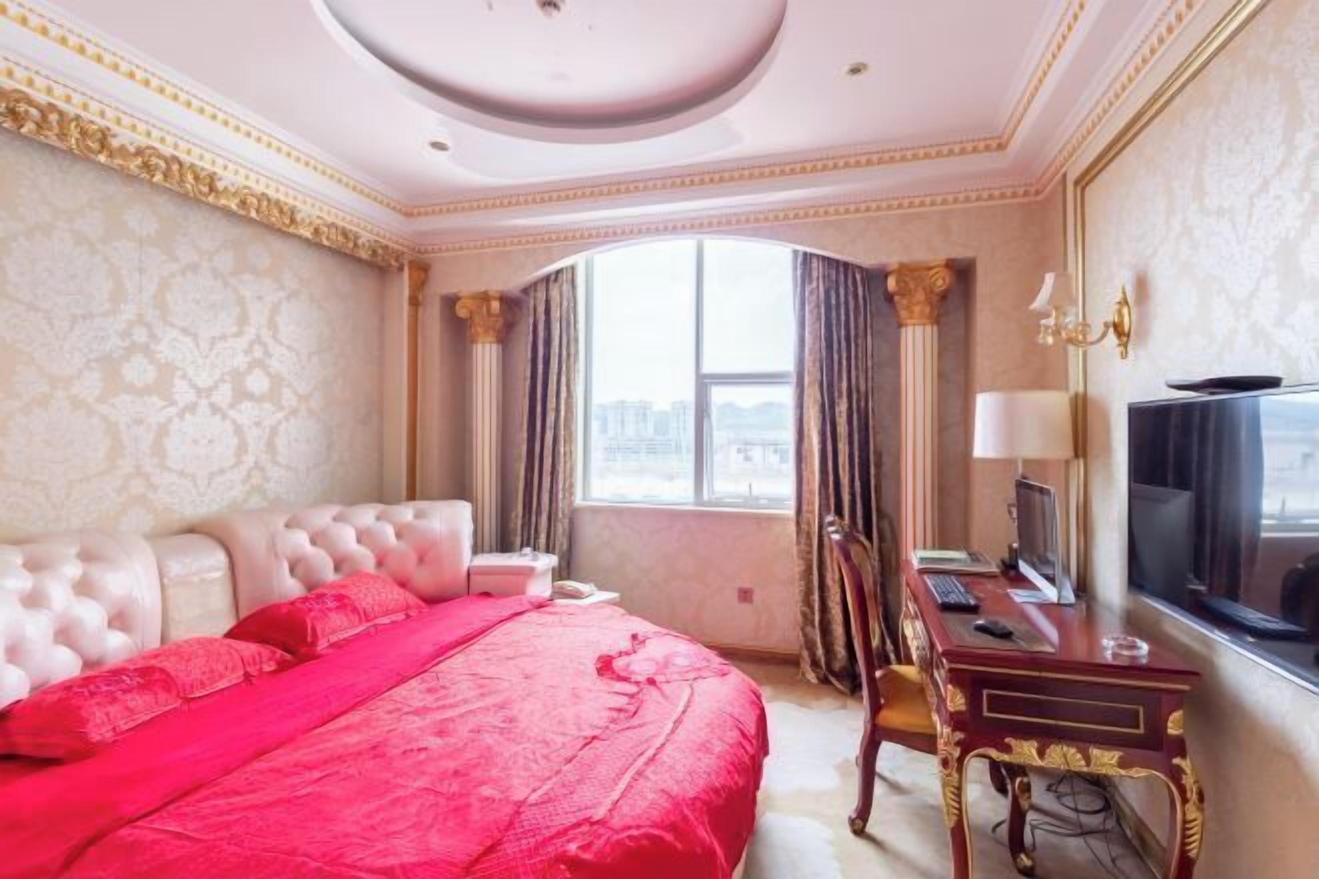 Quarto de hotel com uma cama grande, uma escrivaninha com computador, televisão e janela com cortinas.