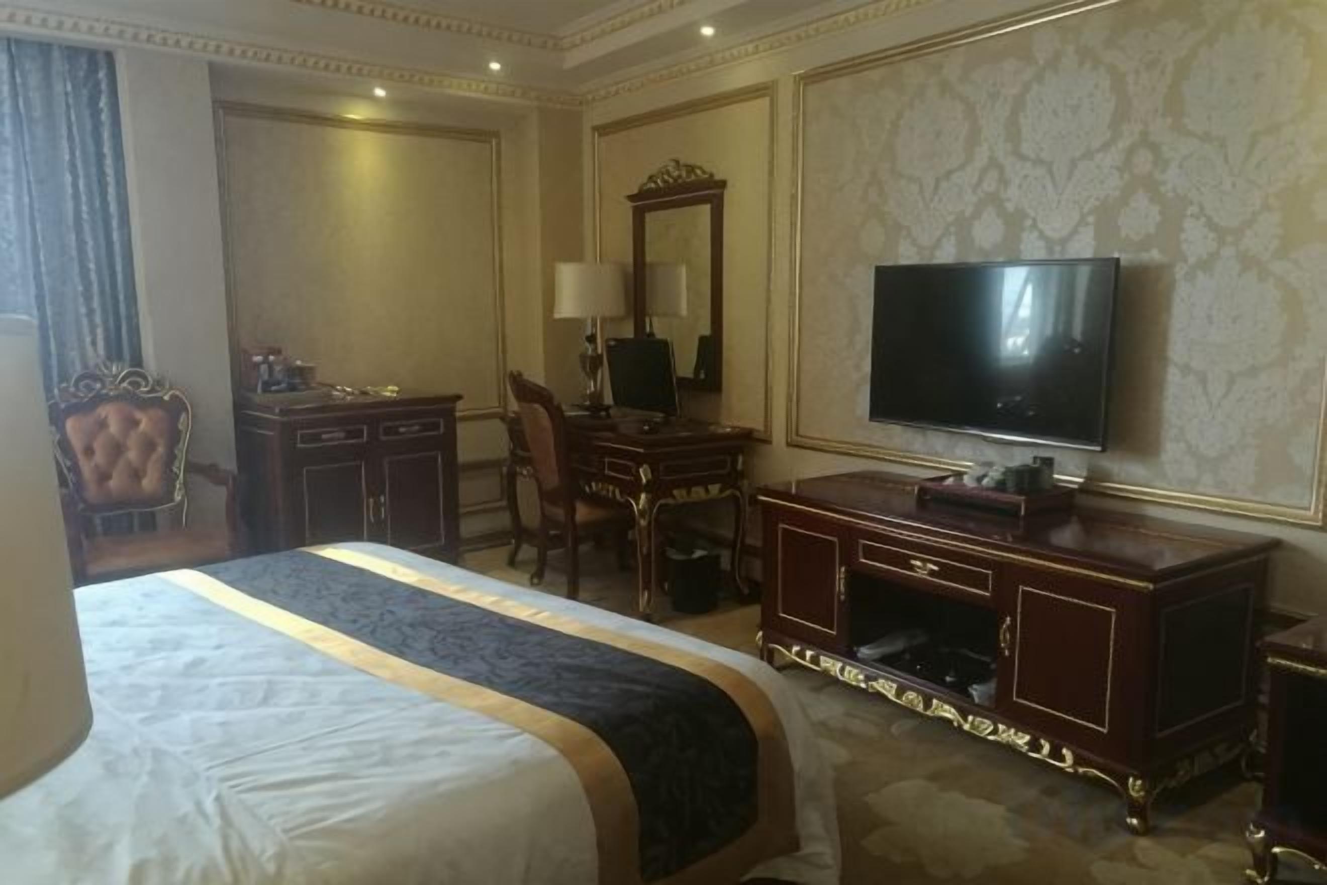 Een hotelkamer met een groot bed, een bureau met stoel, een televisie en een kledingkast.