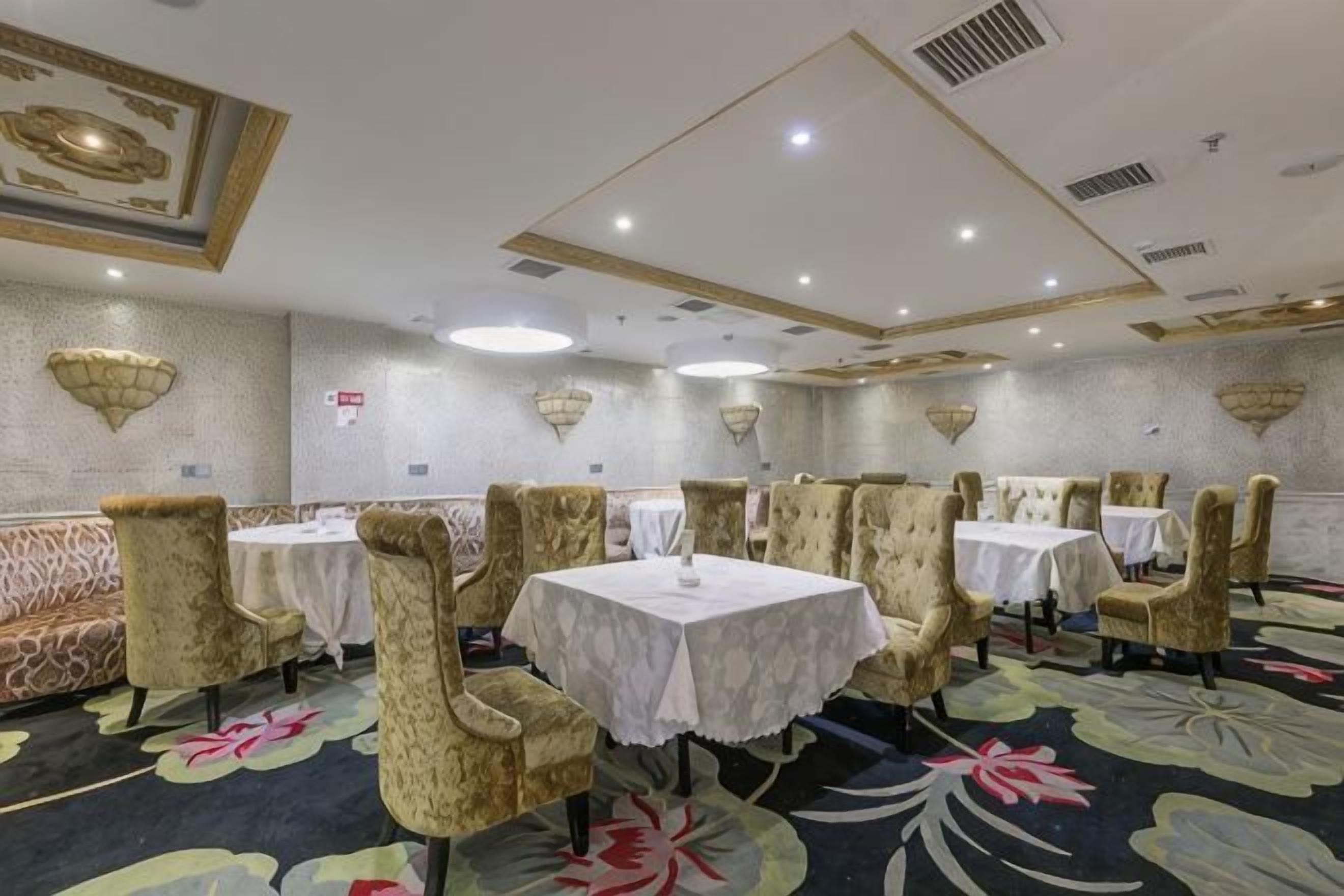 A banquet hall with round tables and cushioned chairs, a patterned carpet, and decorative wall sconces.