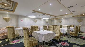 A banquet hall with round tables and cushioned chairs, a patterned carpet, and decorative wall sconces.