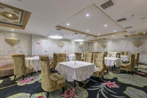 A banquet hall with round tables and cushioned chairs, a patterned carpet, and decorative wall sconces. - Yifeng Hotel (Yifeng)