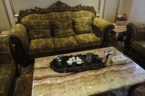 Una habitación con un sofá estampado, una mesa de centro de mármol con una bandeja y una mesita con un florero.