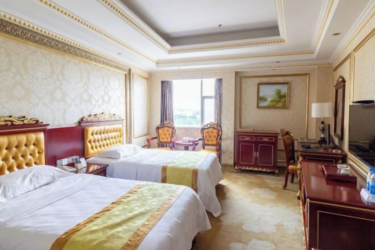 A hotel room with two beds, a desk, a chair, a TV, and a window with a view.