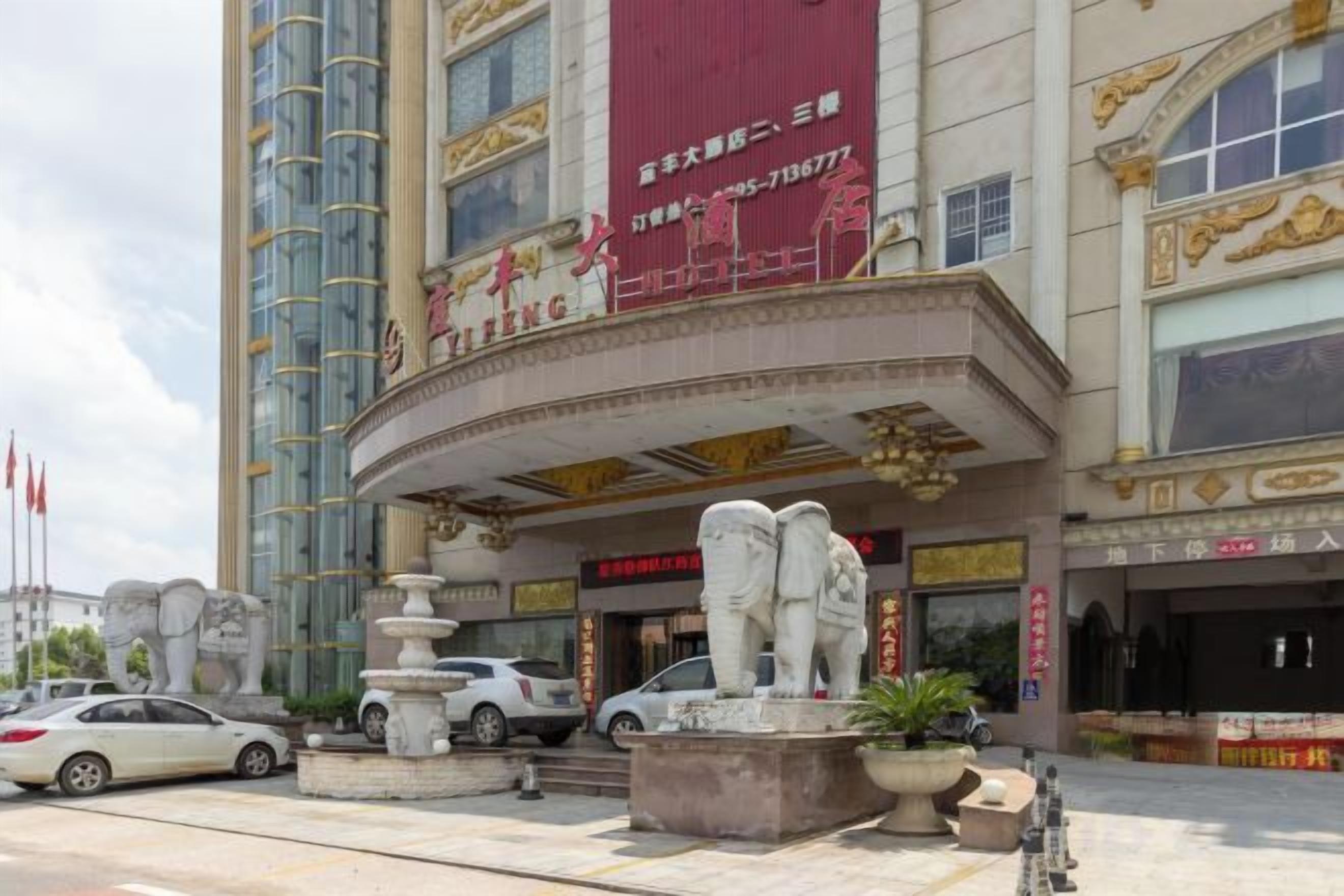 A hotel with a prominent red sign, a fountain, and a statue in front.