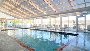 Ein Hallenbad mit großen Glaswänden, gefliestem Boden und Blick ins Freie.