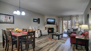 Ein Wohnzimmer mit Kamin, einer Essecke mit Tisch und Stühlen, einem Fernseher über dem Kamin und einem roten Sofa.