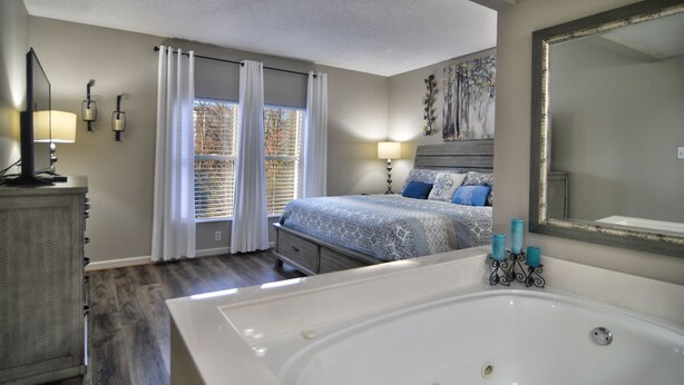 Ein Schlafzimmer mit einem großen Bett, ein Badezimmer mit einer Badewanne und ein Fenster mit Vorhängen.