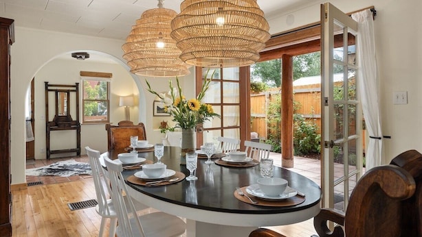 Un coin repas avec une table ronde dressée pour quatre personnes, entourée de chaises blanches. Deux grands luminaires suspendus en forme de globe ornent le plafond.