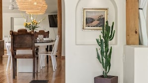Un coin repas avec une table et des chaises en bois, un luminaire suspendu, une plante en pot (un cactus) et un tableau encadré au mur.