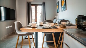 Una cuina moderna amb taula de menjador preparada per a dues persones, un televisor fixat a la paret i quadres penjats a les parets.