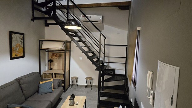 A modern living room with a staircase, a sofa, a coffee table, and a bookshelf. - Description (Granada)