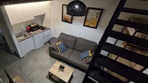 A compact living space with a kitchenette, a sofa with cushions, a coffee table, and a staircase. - Description (Granada)