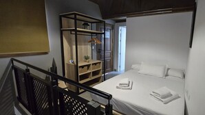 A bedroom with a bed, a wooden shelf unit, and a staircase. - Description (Granada)