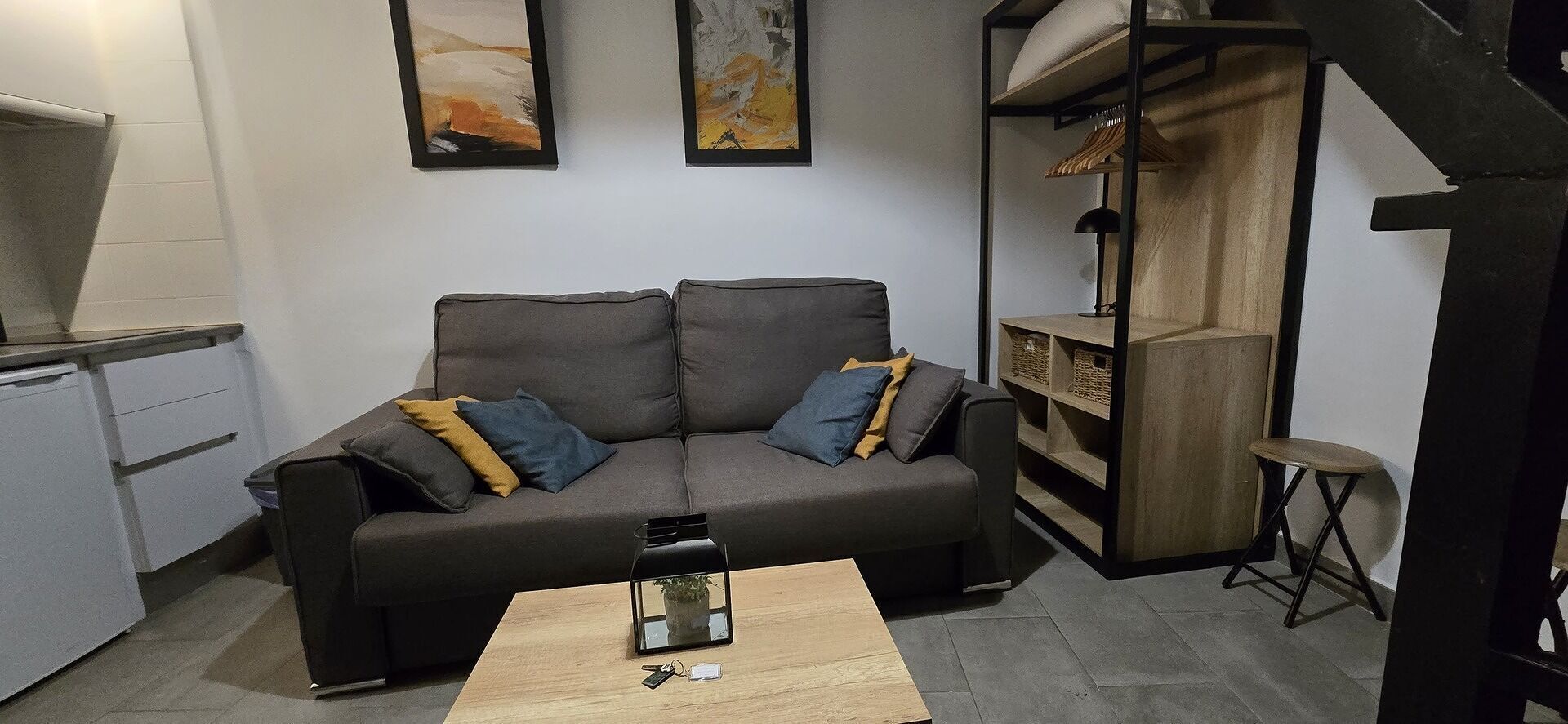 Un espacio habitable pequeño con un sofá gris, una mesa de centro de madera y una estantería.