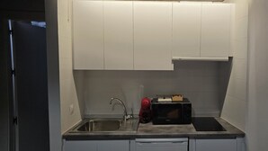 A compact kitchen with a stainless steel sink, a black microwave, and a small countertop. - Description (Granada)