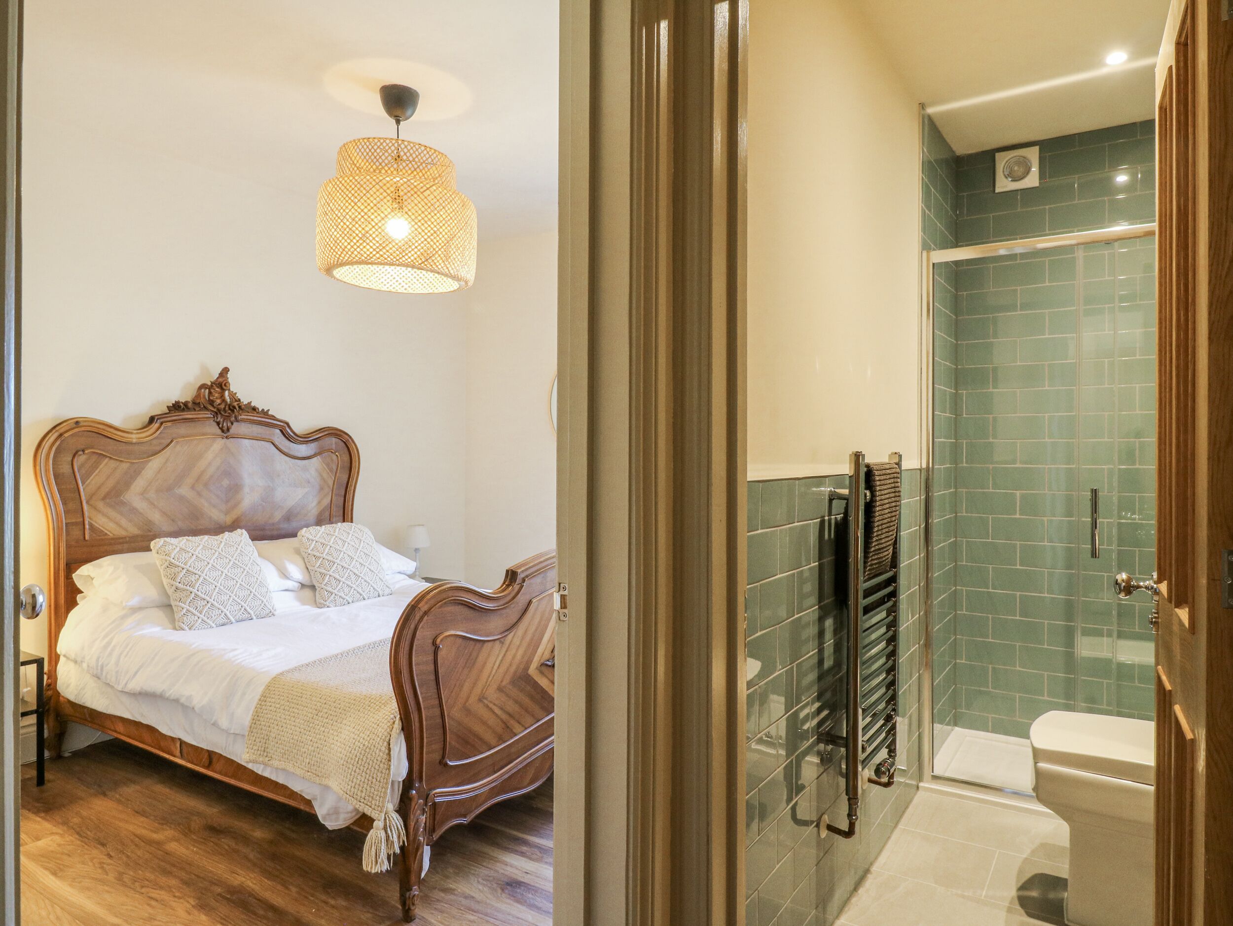 A bedroom with a wooden bed and a hanging light fixture, and a bathroom with a glass shower enclosure and a tiled wall.