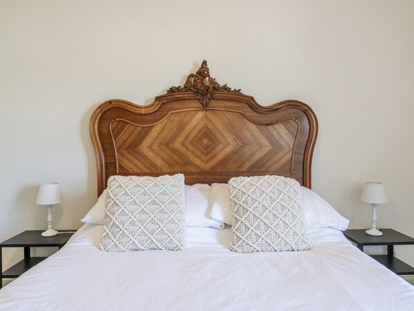 Una cama con cabecera de madera, dos almohadas blancas y dos mesitas de noche con lámparas.