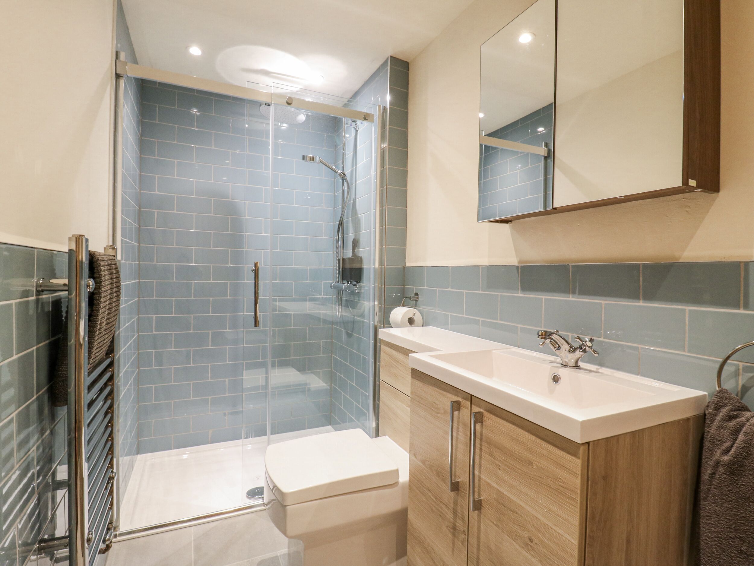 Un baño moderno con cabina de ducha de vidrio, inodoro blanco y tocador de madera con lavamanos.