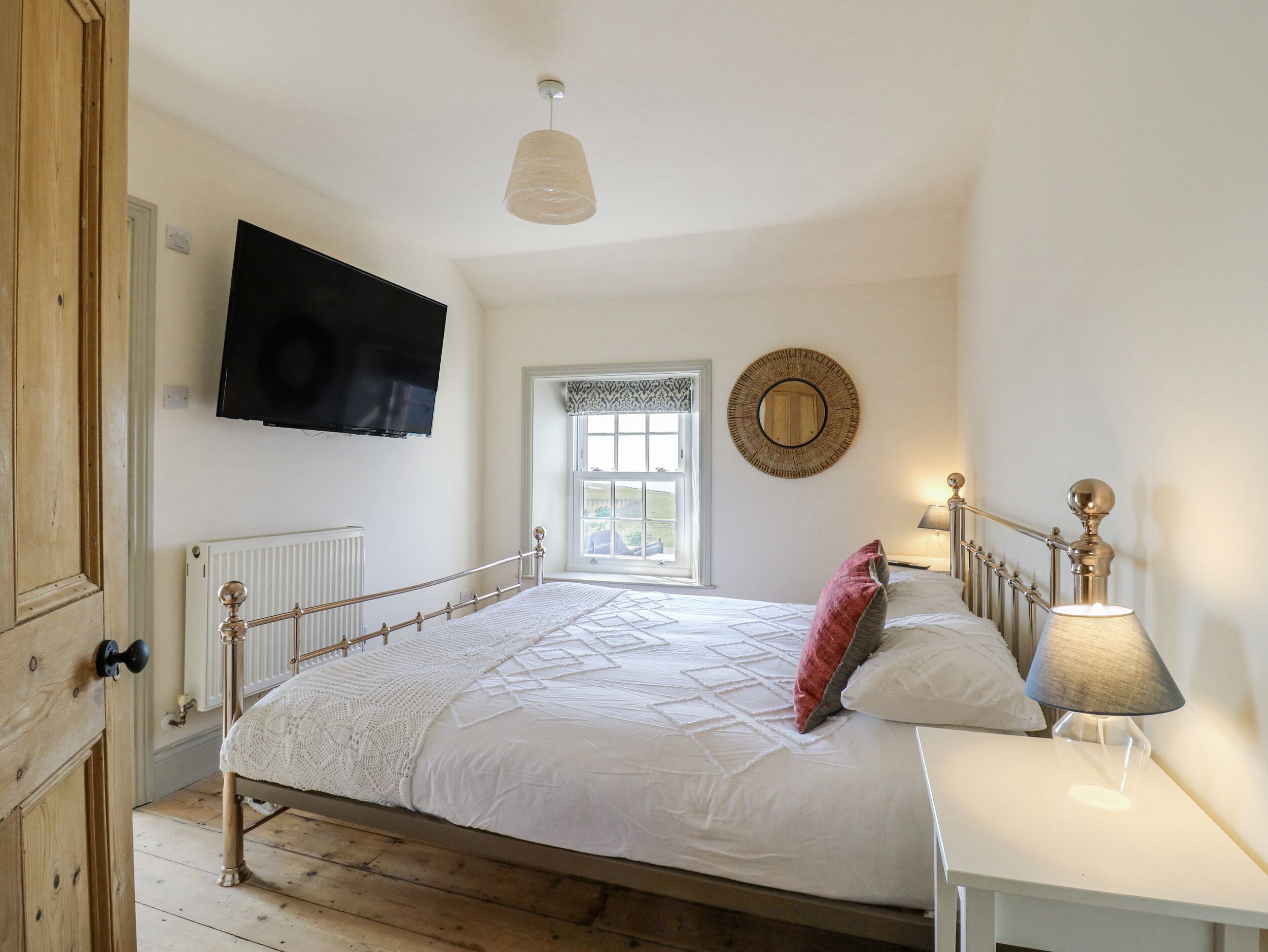 Una camera da letto con un letto, una TV a parete, una finestra vista, una lampada da comodino e un pavimento in legno.