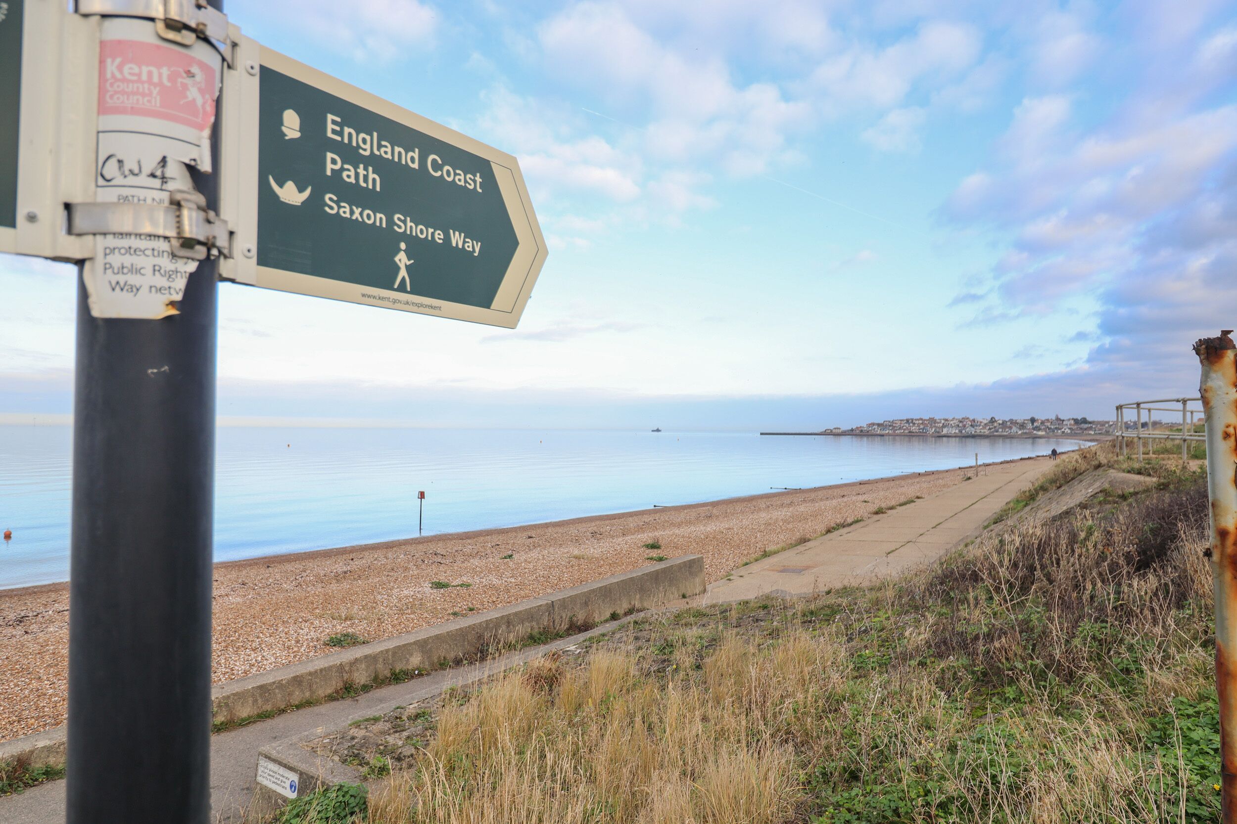 Señal direccional del Sendero Costero de Inglaterra y la Vía de la Orilla Sajona, un camino costero con vista al mar y a una playa.