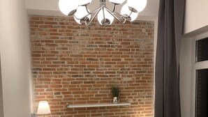Un dormitorio con pared de ladrillo, una araña, una mesita de noche con lámpara, una ventana con cortinas y una cama con almohadas y una colcha.