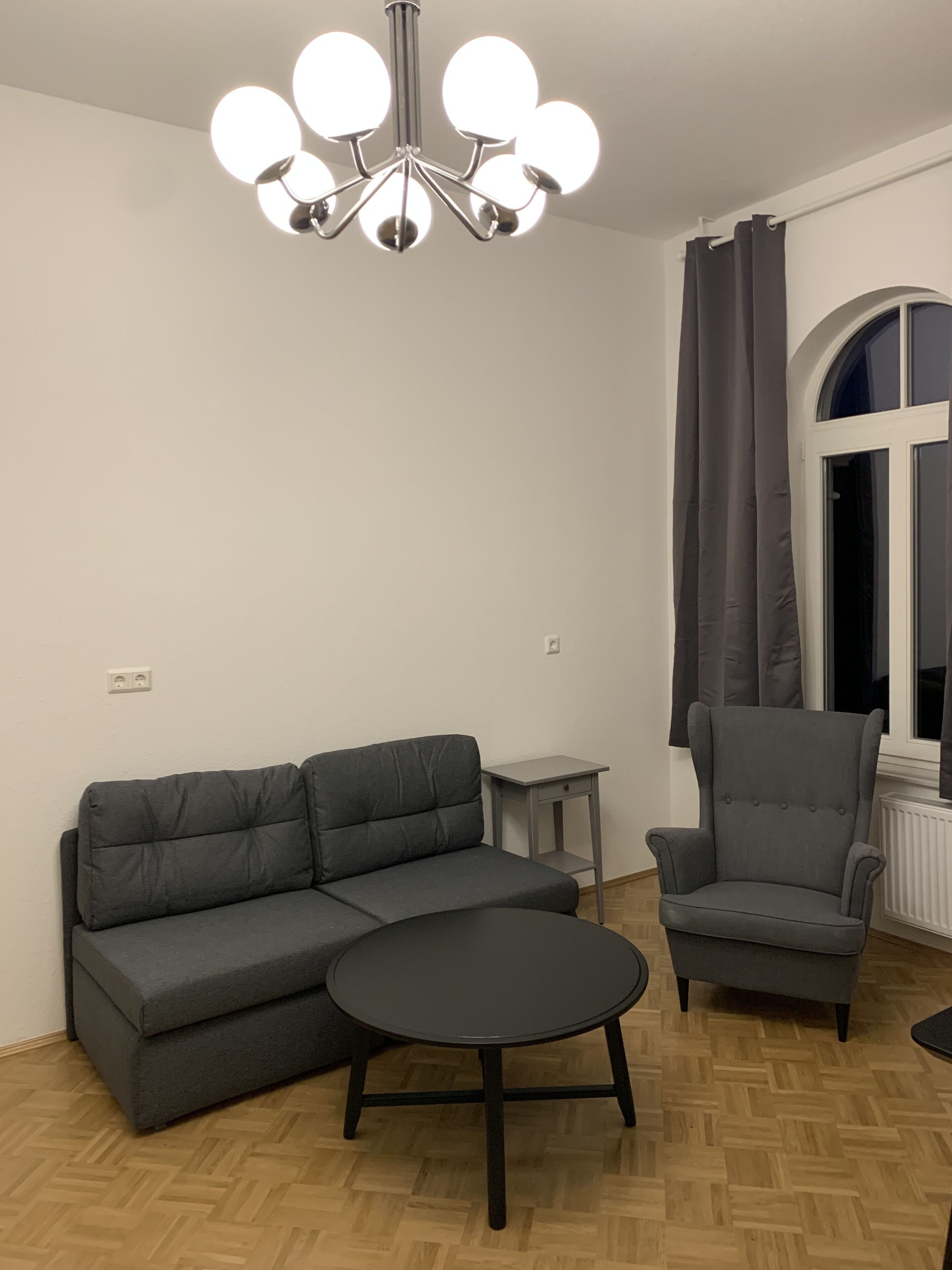 Un salon avec un canapé d’angle gris, une table basse ronde, un fauteuil gris et un lustre moderne.