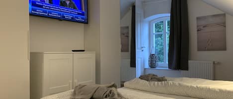 Habitación de hotel con dos camas, un televisor montado en la pared, una ventana con cortinas y un radiador.